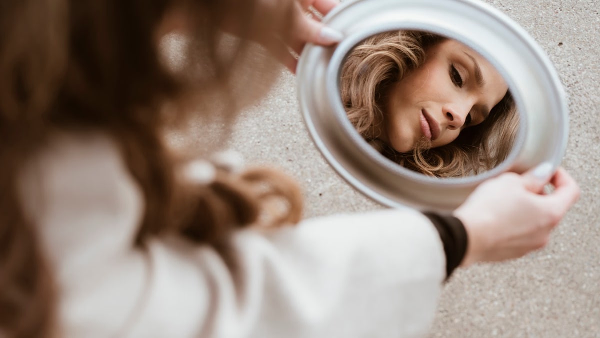 A woman's reflection in a mirror on a city pavement, showing beauty and introspection.